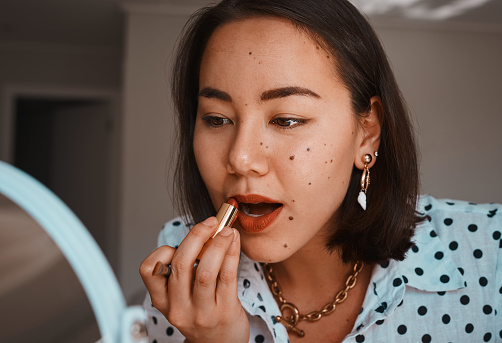 Shot of a beautiful young woman applying lipstick during her beauty routine at home