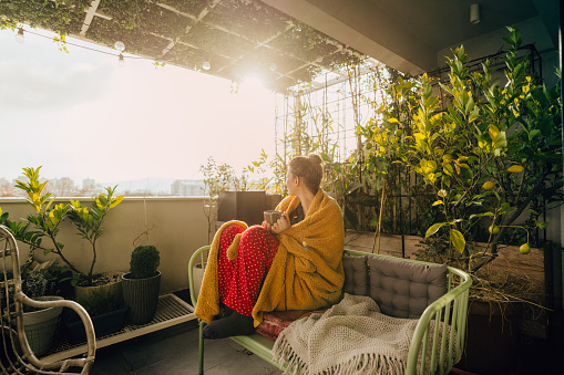 Photo of a young woman having a relaxing start of a day on her terrace, soaking in the first springtime sun and having a hot cup of tea