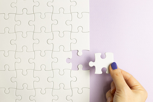Set of white puzzle pieces and hand holding last one piece on purple background. top view