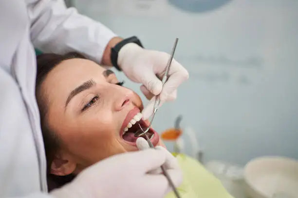 Young male dentist using angled mirror and dental probe for dental scrutiny, on his female patient during her monthly dental appointment