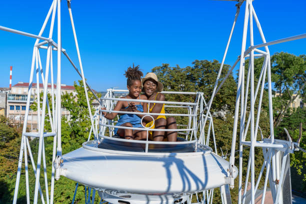 una linda niña afroamericana se está divirtiendo con su madre feliz en entertainment park. - carousel merry go round child african descent fotografías e imágenes de stock