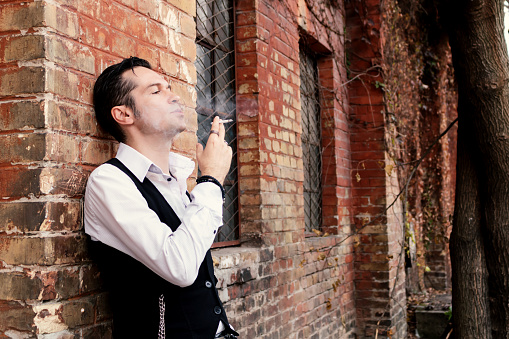 Portrait of pensive man smoking cigarette while leaning on a wall