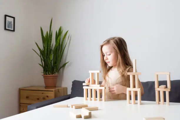 kids playing with wooden jenga constructor. girl builds towers from toy rectangular blocks. concept of developing fine motor skills, games. Leisure activities for children at home.