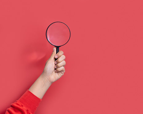 Hand holding magnifying glass on red background