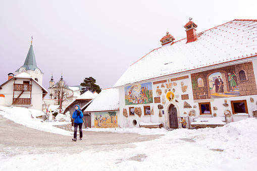 Litija, Slovenia - January 16, 2021: Tourist, mature woman,  walking trough complex of buildings with paintings, from Mother of God church from 13 century on Saint Hill from Zasavje (Zasavska Sveta gora) at 852 m high hill. It is located on the left side of the river Sava, Slovenia.