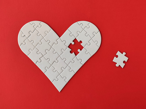 Heart shaped white jigsaw puzzle on red background, a missing piece of the heart puzzle