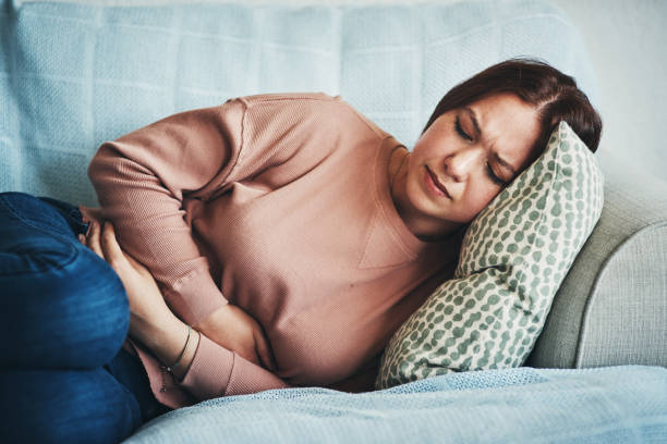 My gut doesn't feel so good Shot of a young woman experiencing stomach pain while lying on the sofa at home Endometriosis stock pictures, royalty-free photos & images