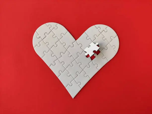 Heart shaped white jigsaw puzzle on red background, puzzle pieces completing the heart shape