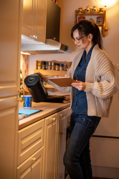 istock Woman holding tablet and pouring tea in the white kitchen. 1300136944