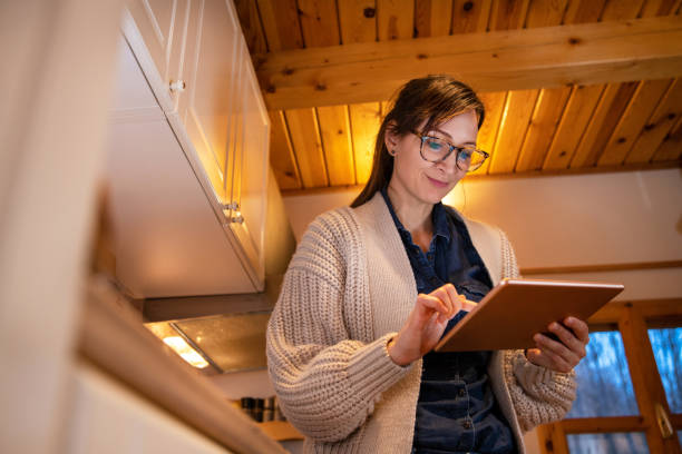 istock Woman with eyeglasses standing in the kitchen, holding digital tablet. 1300137900