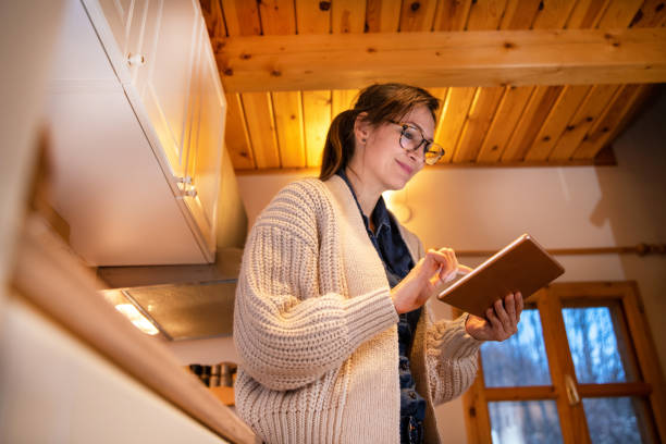 Woman standing in the kitchen, holding digital tablet.