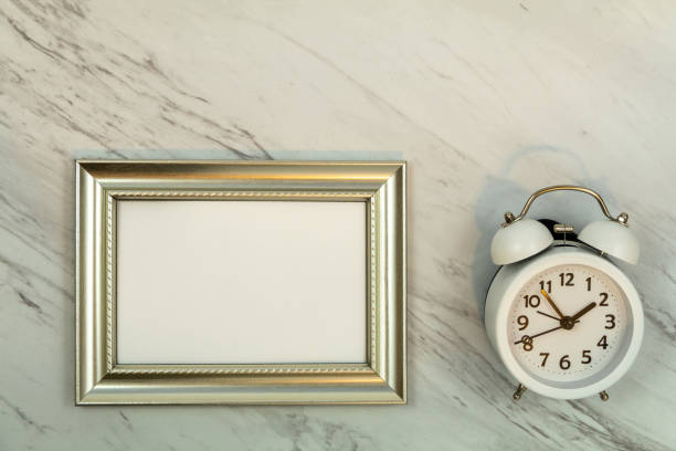 istock Metallic photo frame mockup on marble white alarm clock flat lay 1300138272