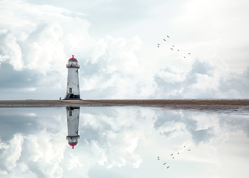 Telacre lighthouse on the coast of North Wales Point of Ayre reflecting a stunning storm sky in a pool of sea water.