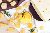 Top view of fresh homemade creamy cheese sauce in a glass bowl with rosemary and parmesan pieces on light background