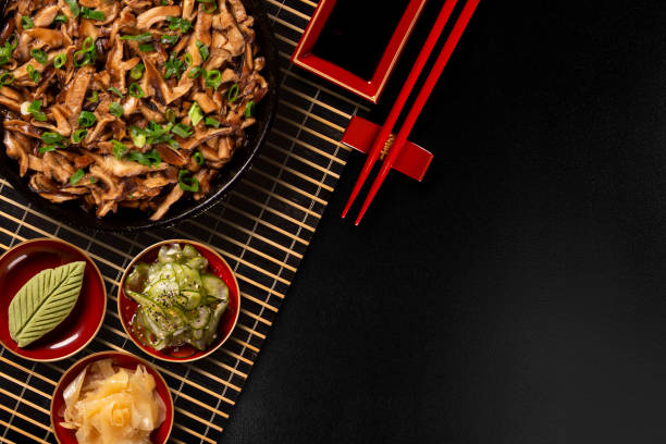 shimeji mushrooms in iron pan with ginger, wasabi and sunomono in a black background.Top View. shimeji mushrooms in iron pan with ginger, wasabi and sunomono in a black background.Top View sunomono stock pictures, royalty-free photos & images