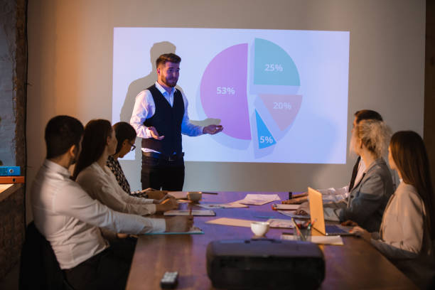 istock Male speaker giving presentation in hall at workshop. Audience or conference hall. Participants, co-workers listening at the table. 1300153555