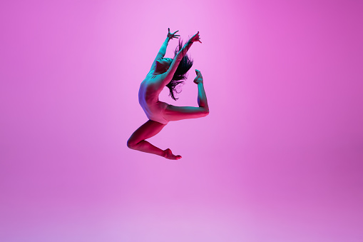 Joven y elegante bailarina de ballet aislada sobre fondo de estudio rosa en luz de neón. Arte, movimiento, acción, flexibilidad, concepto de inspiración. photo
