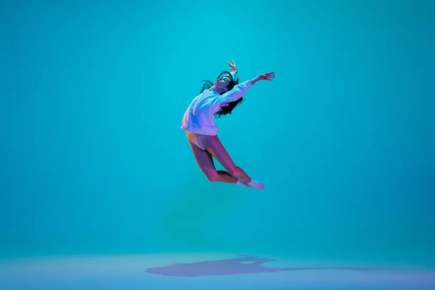 istock Young and graceful ballet dancer isolated on blue studio background in neon light. Art, motion, action, flexibility, inspiration concept. 1300154890