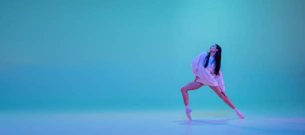 istock Young and graceful ballet dancer isolated on blue studio background in neon light. Art, motion, action, flexibility, inspiration concept. 1300154907
