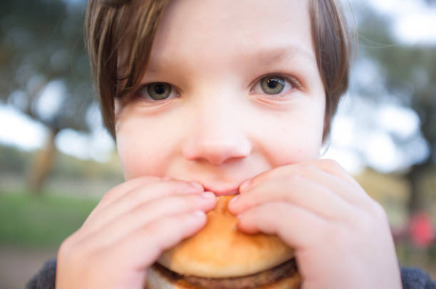 istock Little boy bites hamburger outdoors 1300155505