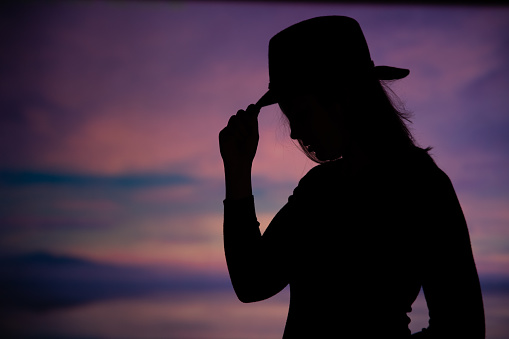Young woman holding a cowboy hat in the pink sunset.