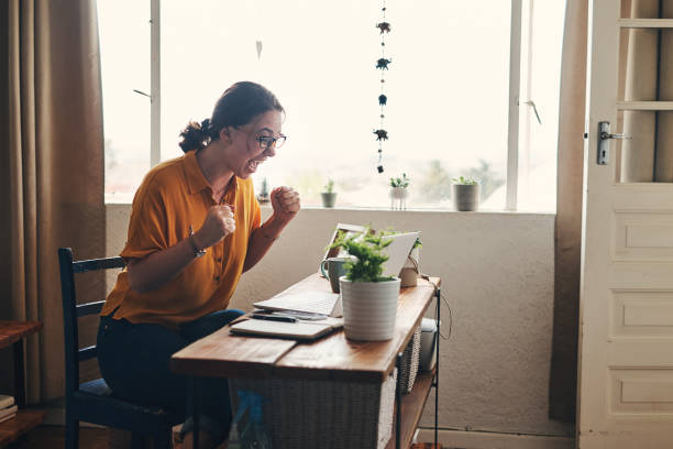 And the customers keep on rolling in Shot of a young woman using a laptop and celebrating while working from home wtf stock pictures, royalty-free photos & images