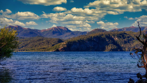 Landscape of Lacar lake at sunset. Taken from Quila Quina beach looking to the blue water lake and the mountains behind, under a blue sky with a few white clouds. Taken on a warm summer afternoon at dusk