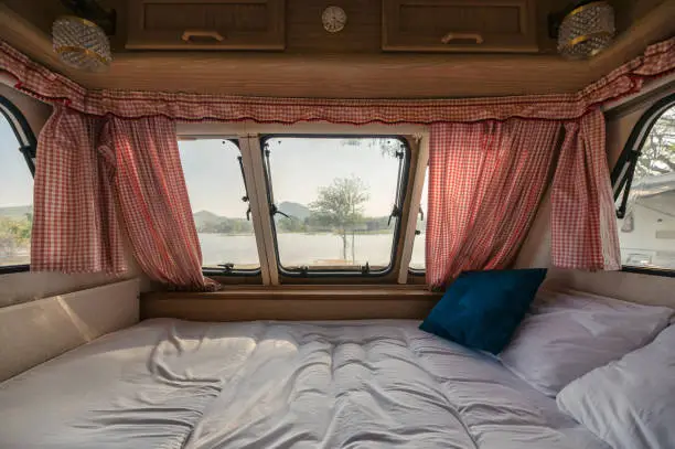 Inside of empty bed in camper van and the view through window with curtain on lakeside at campsite