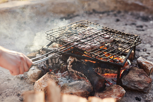 Cropped shot of an unrecognizable man grilling meat on an outdoor fire