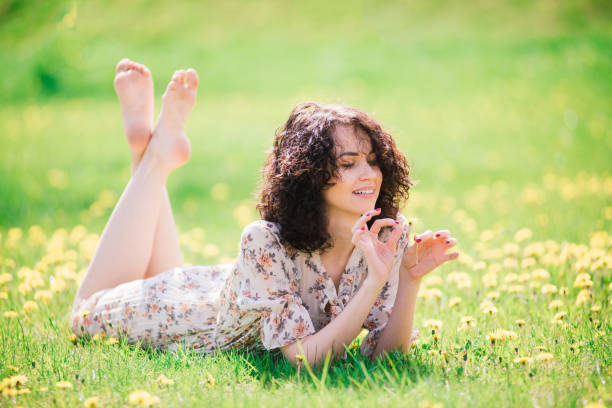 Young attractive woman with curly long hair posing in spring blooming garden, apple trees Young attractive woman with curly long hair posing in spring blooming garden floral dress stock pictures, royalty-free photos & images