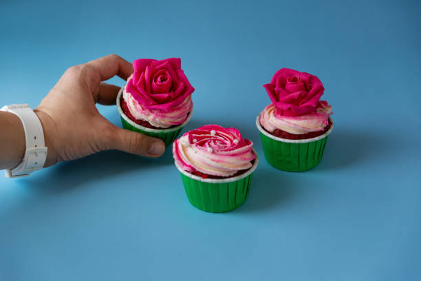 istock A woman's hand takes appetizing cupcakes with pink cream on a blue background 1300168937