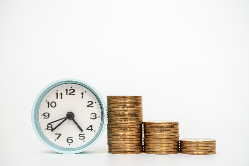 Business, Money and Saving and Time Concept. Closeup stack of gold coins with old vintage round clock on white background.