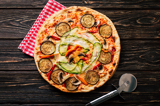 Vegetable pizza with mushrooms, zucchini and eggplant on a wooden background.
