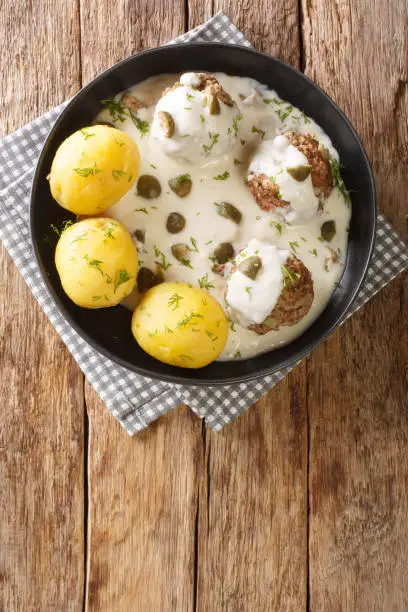 Konigsberger Klopse, also known as Sobklopse are a German specialty of meatballs in a white sauce with capers close-up in a plate on the table. vertical top view above