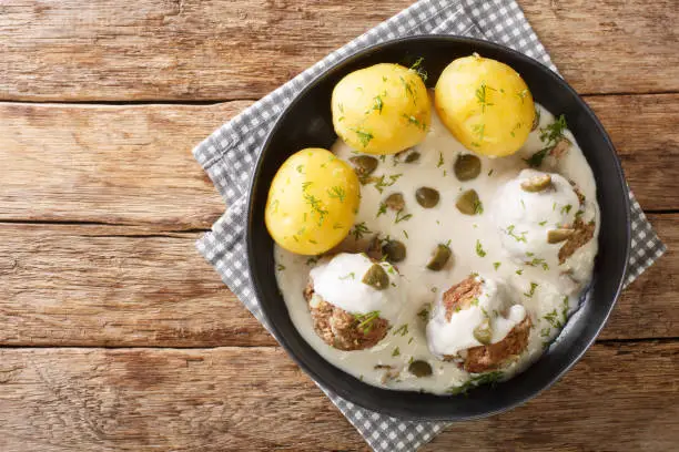 Delicious German meatballs in caper sauce served with boiled potatoes close-up in a plate on the table. Horizontal top view above