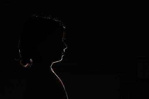 Black foreground and background with backlit silhouette of boy with shoulder length shaggy hair looking straight ahead with hair back