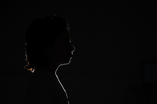 Black foreground and background with backlit silhouette of boy with shoulder length shaggy hair head tilted up ahead with hair back