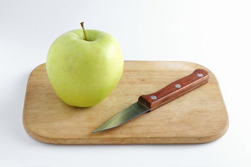 Green apple and knife on cutting board on white background