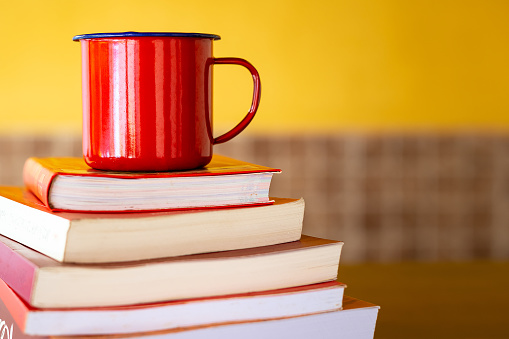 Several books stacked with red mug.