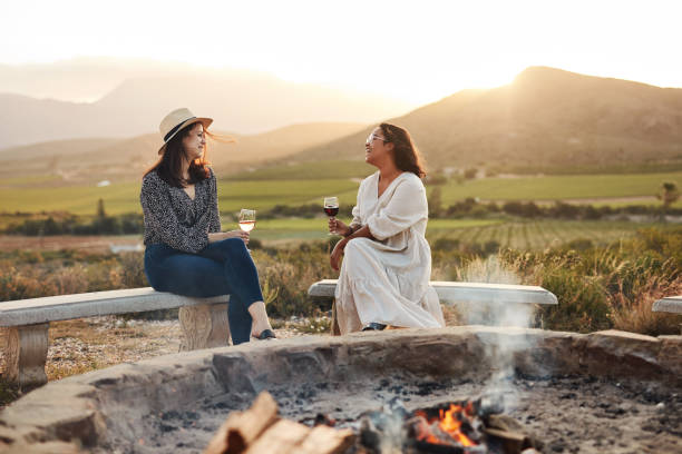 Enjoying a much needed break Shot of two women drinking wine while sitting by a fire pit wine tasting stock pictures, royalty-free photos & images
