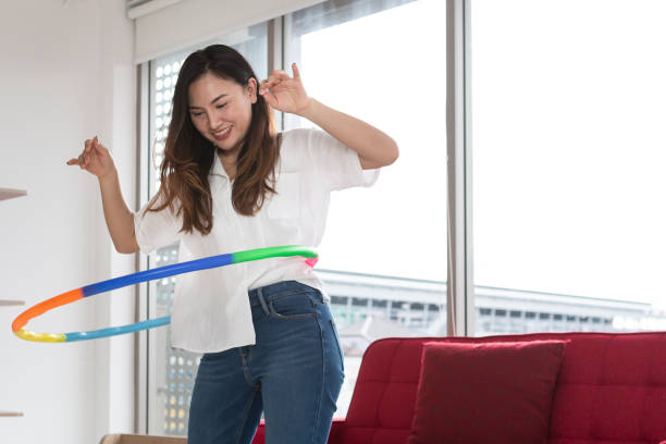 mujeres asiáticas felices jugando hula hoop en la sala de estar en casa. joven adulta aprendiendo a jugar con un hula-hoop en una sala de estar. - hooping fotografías e imágenes de stock