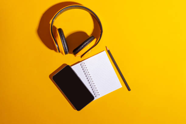 istock Desktop with yellow wireless headphones and an open notebook on a bright yellow background 1300183634