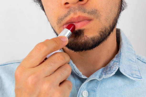 istock Non-binary bearded young Hispanic man on a white background putting red lipstick on his lips 1300184681
