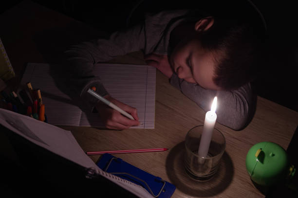 Tired schoolboy with candle in complete darkness doing homework. Power outage, blackout, concept image. Tired schoolboy with candle in complete darkness doing homework. Power outage, blackout, concept image. blackout photos stock pictures, royalty-free photos & images