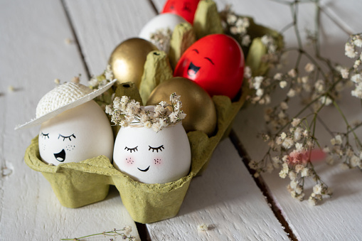 Minimalist Easter decoration on Easter eggs. Eggs are smiley, beautiful and cute. They are placed in green egg container surrounded by small white dry flowers.