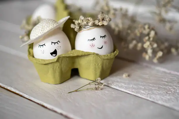 Minimalist Easter decoration on white Easter eggs. Eggs are smiley, beautiful and cute. They are placed in green egg container surrounded by small white dry flowers.