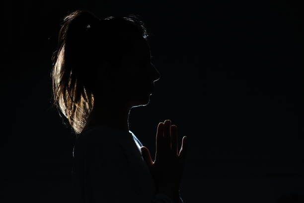 istock Silhouette of attractive women with ponytail looking forward with prayer hands 1300189129