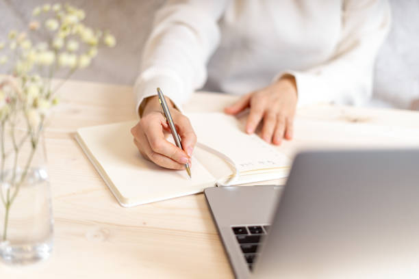istock Woman writes in notebook on desk with laptop 1300191897