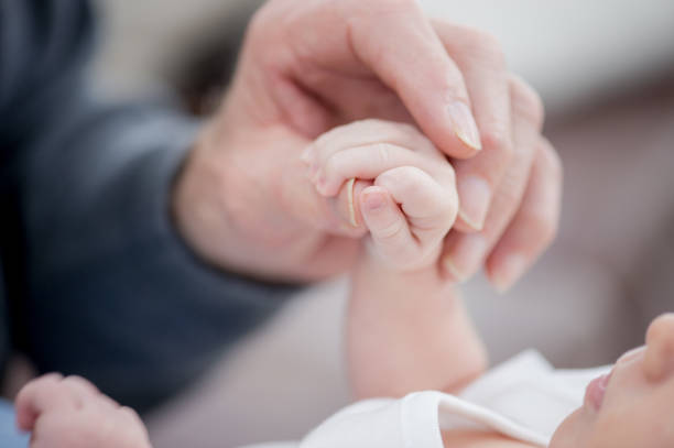 The concept of a happy family, on the tender palm of the father, put the palm of the newborn baby, mother gently supports the little hand of her son, who lies on her lap, mother and son are dressed in white clothes