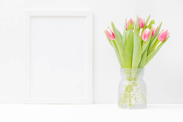 istock Home interior with decor elements. Mockup with a white frame and pink tulips in a vase on a light background 1300195393